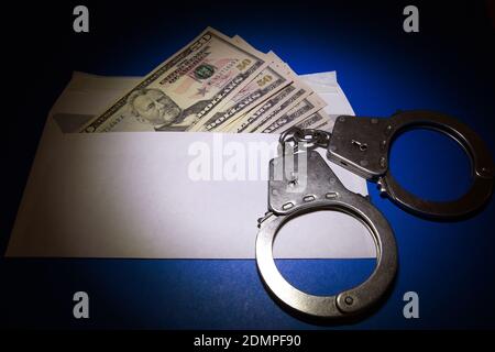 Handschellen auf dem Umschlag mit einem American Dollars auf dem Blauer Papierhintergrund im Dunkeln Stockfoto