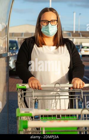 Eine Frau, die eine Gesichtsmaske trägt und einen Einkaufswagen aus einem Trolley-Park in Schottland zieht. Stockfoto