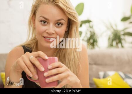 Wunderschöne blonde haarige Frau lächelt die Kamera spielerisch halten tasse Kaffee entspannen im lokalen City Cafe Copyspace Weiblichkeit Sinnlichkeit SED Stockfoto