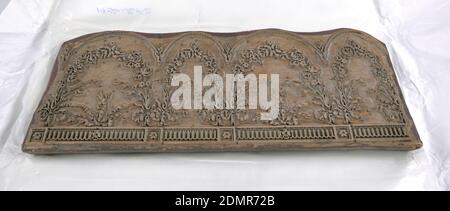 Holzblock, Holz, Messing, rechteckiger Block, bestehend aus fünf Lagen Schichtholz, von denen die obere geschnitzt ist. An der Spitze, Bögen, die auf die Flutung, abwechselnd mit Rosetten. Unten zwei große und zwei kleine Jakobsmuscheln; restliche Fläche gefüllt mit Rosensücken und Schleifen von Bändern. Zweiter Block von einem Satz von drei. (1956-164-1 und -3)., Frankreich, 1860–70, Wandverkleidungen, Holzblock Stockfoto