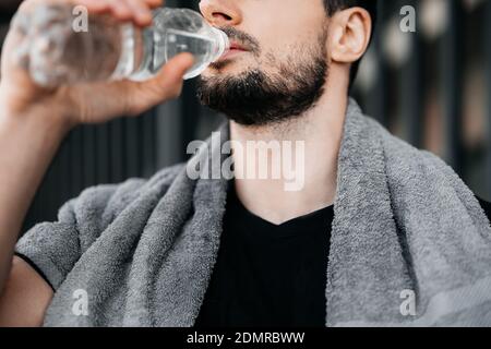 Mann Trinkwasser aus Plastikflasche nach hartem Training. Nahaufnahme Schnittansicht des männlichen Gesichts. Vergessen Sie nicht, während des Trainings zu trinken. Passen Sie auf sich auf Stockfoto