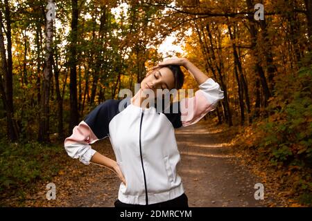 Frau Athlet wärmt Hals vor dem Training. Joggen im Herbstpark. Herbstkonzept. Gesunder Lebensstil. Kaukasische Frau in schwarz und weiß Stockfoto