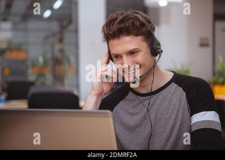 Junger gutaussehender Mann, der im Callcenter arbeitet, Headset mit Mikrofon trägt, Platz zum Kopieren. Freundlicher männlicher Kundendienstbetreiber, der Anrufer beantwortet, Typ Stockfoto