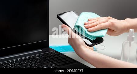 Weibliche Hände desinfizieren Telefonbildschirm und Laptop-Tastatur mit Alkoholdesinfektionsmittel. Schutz Hygiene Prävention vor Infektionen, Keime, Bakterien durch Stockfoto