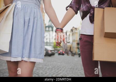 Kurzer Schuss von zwei Frauen, die Hand halten und mit Einkaufstaschen durch die Stadt gehen. Weibliche Freunde genießen Sightseeing in ihrem Urlaub, Hände halten Stockfoto