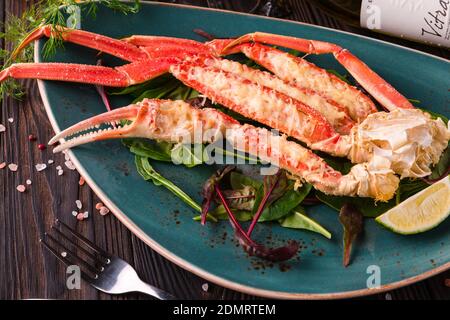 Krabbenbeine mit frischen Zitronenscheiben auf einem grünen Teller auf dunklem Holzhintergrund. Bereit zum Essen. Stockfoto