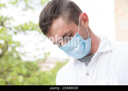 Young man looking depressed, wearing medical protective mask on a walk outdoors in the park Stockfoto