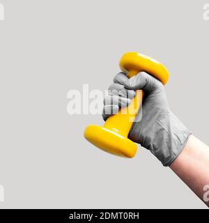 Hand in grau Handschuh halten gelbe Hantel. Ohne Quarantäne, zu Hause bleiben, trainieren. Speicherplatz kopieren. Stockfoto