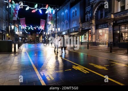 Zwei Frauen gehen in Cardiff während der Weihnachtszeit eine ruhige High Street mit sozialen Distanzschildern entlang. Stockfoto