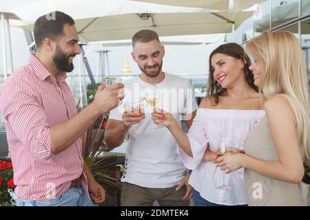 Group of friends chatting joyfully, having drinks at rooftop bar Stock Photo