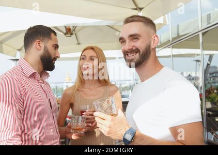 Attraktiver junger Mann, der lächelt und fröhlich auf der Sommerdachparty an der Bar schaut Stockfoto