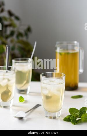 Kalter, erfrischender grüner Tee mit Eis und Minze, Teekanne und Gläser auf weißem Holzhintergrund Stockfoto