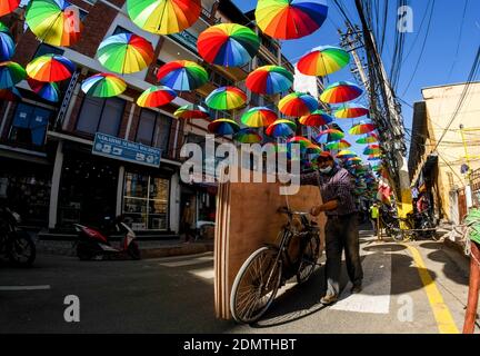 A man carry boards on his bicycle walks under colourful hanging  umbrellas in Sankata Temple area. Stock Photo