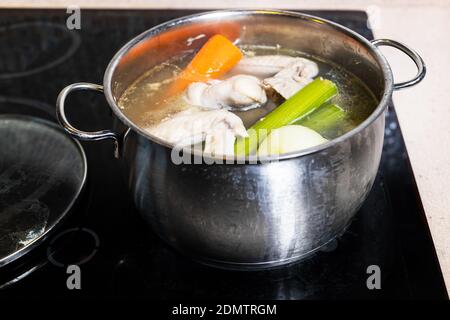 Hühnerflügelsuppe wird in Stahlstedpot auf Herd gekocht Zu Hause Küche isoliert auf weißem Hintergrund Stockfoto