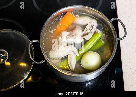 Draufsicht auf Hähnchenflügel Brühe ist in Stahl gekocht Stewpot auf Herd zu Hause Küche isoliert auf weißem Hintergrund Stockfoto