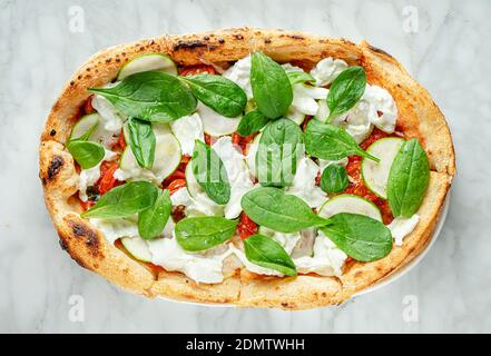 Römische Pizza mit Spinat, Zucchinischeiben, Stracciatella-Käse und Tomaten auf Marmorboden. Italienisches Essen, Overhead Stockfoto