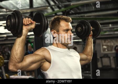 Pumpen Sie es auf! Junge gutaussehende seriöse Fitness-Mann tun Gewichtheben Übungen mit Hanteln im Fitnessstudio Motivation Herausforderung sportliche Ziele erreichen Stockfoto