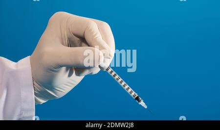 Spritze in die Hände des Arztes mit Handschuhen und blauem Hintergrund Stockfoto