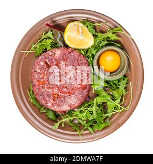 top view of Steak tartare (raw minced beef meat) and yolk in bowl on fresh greens on brown plate isolated on white background Stock Photo