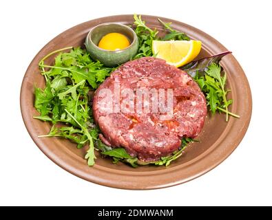 portion of Steak tartare (raw minced beef meat and raw yolk in bowl on fresh greens) on brown plate isolated on white background Stock Photo