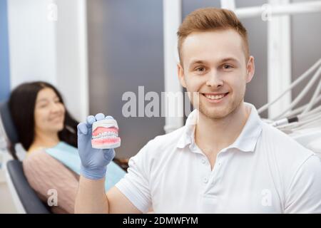 Er kümmert sich um Ihre Gesundheit. Fröhliche professionelle Zahnarzt lächelt an der Kamera hält Zahnform seinen Patienten auf dem Rücken Copyspace Gesundheit sitzen Stockfoto