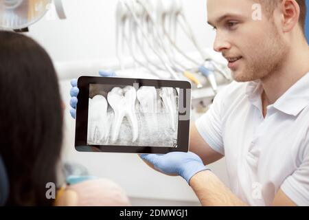 This is the issue. Handsome male dentist using digital tablet while working with his client showing x-rays on the display consultation problems operat Stockfoto
