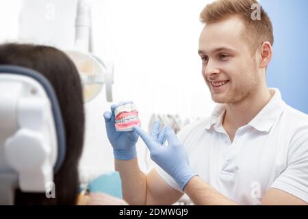 Ihr Zahnarzt. Professionelle männliche Zahnarzt lächelnd im Gespräch mit seinem Kunden zeigt eine Zahnform Gesundheitsberatung Beratung Beratung Termin Zahn Stockfoto