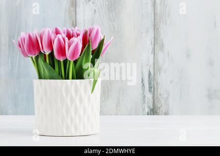 Rosa Tulpen in weißer Keramikvase, blauer Holzhintergrund. Stockfoto