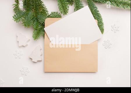 Weihnachts-Grußkarte mit Umschlag auf weißem Hintergrund mit Tannenzweigen und fröhlichen Neujahr Dekorationen. Copyspace der Draufsicht Stockfoto