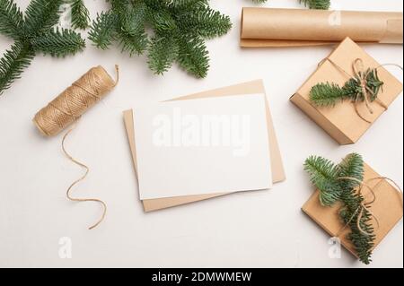 Weihnachtsmockup Grußkarte mit Umschlag auf weißem Hintergrund mit Tannenzweigen und fröhlichen Neujahr Dekorationen. Copyspace der Draufsicht Stockfoto