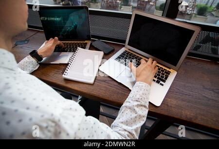 Konzentrierter Mann arbeitet auf seinen Laptops. Erfolgreiche männliche Freiberufler Wetten an der Börse. Café im Hintergrund. Konzept der Finanzkompetenz. Blau Stockfoto