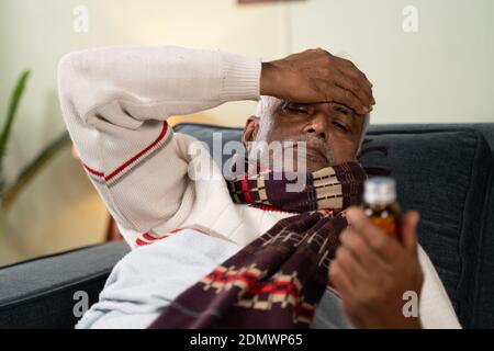 Kranker alter Mann besorgt über die Einnahme von Pillen durch die Hand Auf dem Kopf, während er auf dem Sofa zu Hause schläft - Konzept der älteren Menschen besorgt über Pillen Seite Stockfoto