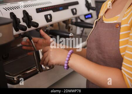 Cropped shot of unrecognizable female barista steaming milk, preparing drinks for customers using coffee machine Stockfoto