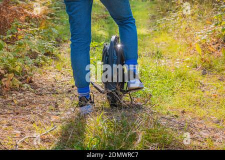 Rückansicht der Frauenbeine auf einem Elektro-Einrad in Der Wald an einem sonnigen Tag Stockfoto