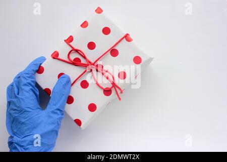 Hand in medizinischen Handschuh mit einem Geschenk. Overhead-Ansicht der verpackten Geschenkbox mit rotem Band auf weißem Hintergrund. Stockfoto