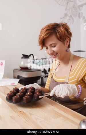Vertikale Aufnahme einer fröhlichen jungen Kellnerin, die köstlich serviert Schokolade vegane Süßigkeiten Stockfoto