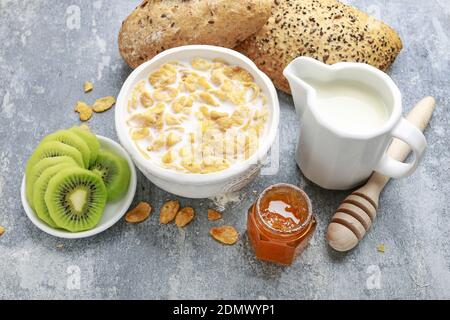 Leckeres und gesundes Frühstück. Auswahl an Speisen auf dem Küchentisch. Milch, Honig, Maisflocken und Kiwi-Scheiben. Stockfoto