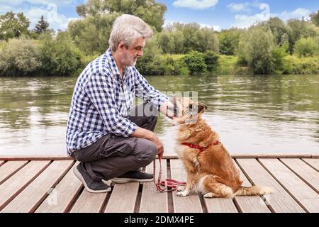 Man and his dog sitting on wooden pier. Holiday with an animal concept. Summer time Stockfoto