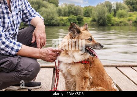 Man and his dog sitting on wooden pier. Holiday with an animal concept. Summer time Stockfoto