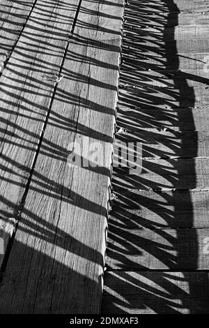 Eine vertikale Graustufenaufnahme der alten Holzplanken und Schatten von Geländern Stockfoto