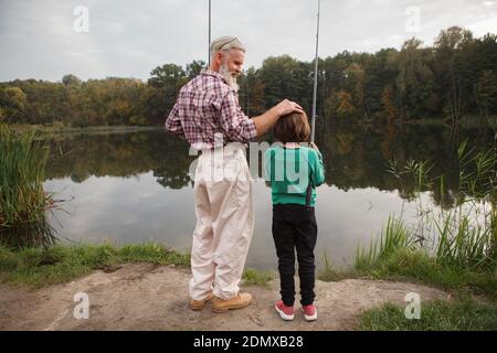 Rückansicht Ganzlängenaufnahme eines stolzen Granpa beobachten Sein Enkel Angeln auf dem See Stockfoto