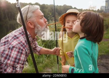 Two cute children playing with their grandpa after fishing together on the lake Stockfoto