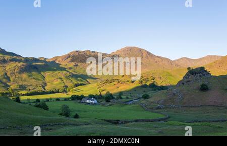 Little Langdale, Cumbria, England. Blick über grüne Felder auf Fell Foot Farm und den Gipfel des Wetherlam, Sonnenaufgang. Stockfoto