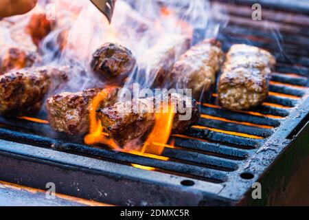 Preparing meat rolls called mici or mititei on barbecue. close up of grill with burning fire with flame and smoke. Stock Photo