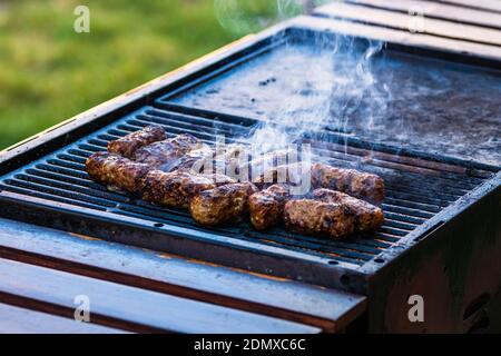 Preparing meat rolls called mici or mititei on barbecue. close up of grill with burning fire with flame and smoke. Stock Photo