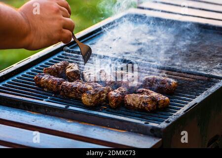 Preparing meat rolls called mici or mititei on barbecue. close up of grill with burning fire with flame and smoke. Stock Photo