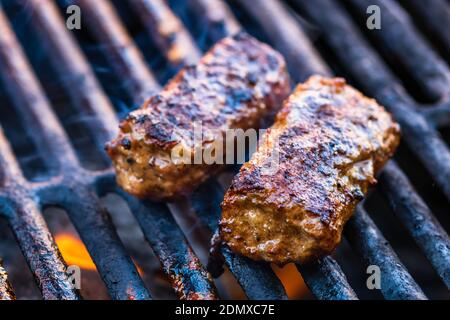 Preparing meat rolls called mici or mititei on barbecue. close up of grill with burning fire with flame and smoke. Stock Photo