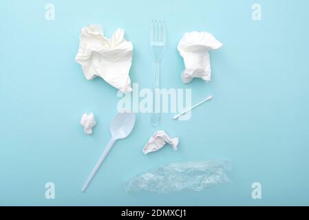 Gebrauchte Plastikgeschirr als Müll, zerknitterte Papierservietten, Baumwollknospen, Löffel, Gabel, Kunststoffverpackung auf blauem Hintergrund, Konzept-Layout Stockfoto