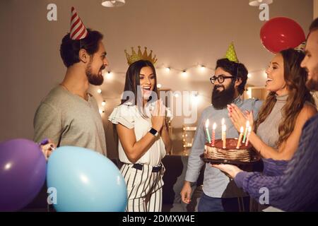 Gruppe von Freunden wünschen alles gute zum Geburtstag der jungen Frau und Geben ihr Geburtstagstorte Stockfoto