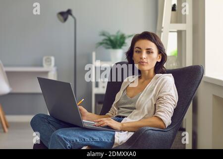 Zwanglose weibliche Managerin, die an einem Laptop arbeitet und in ihrem Büro auf einem Stuhl sitzt. Stockfoto